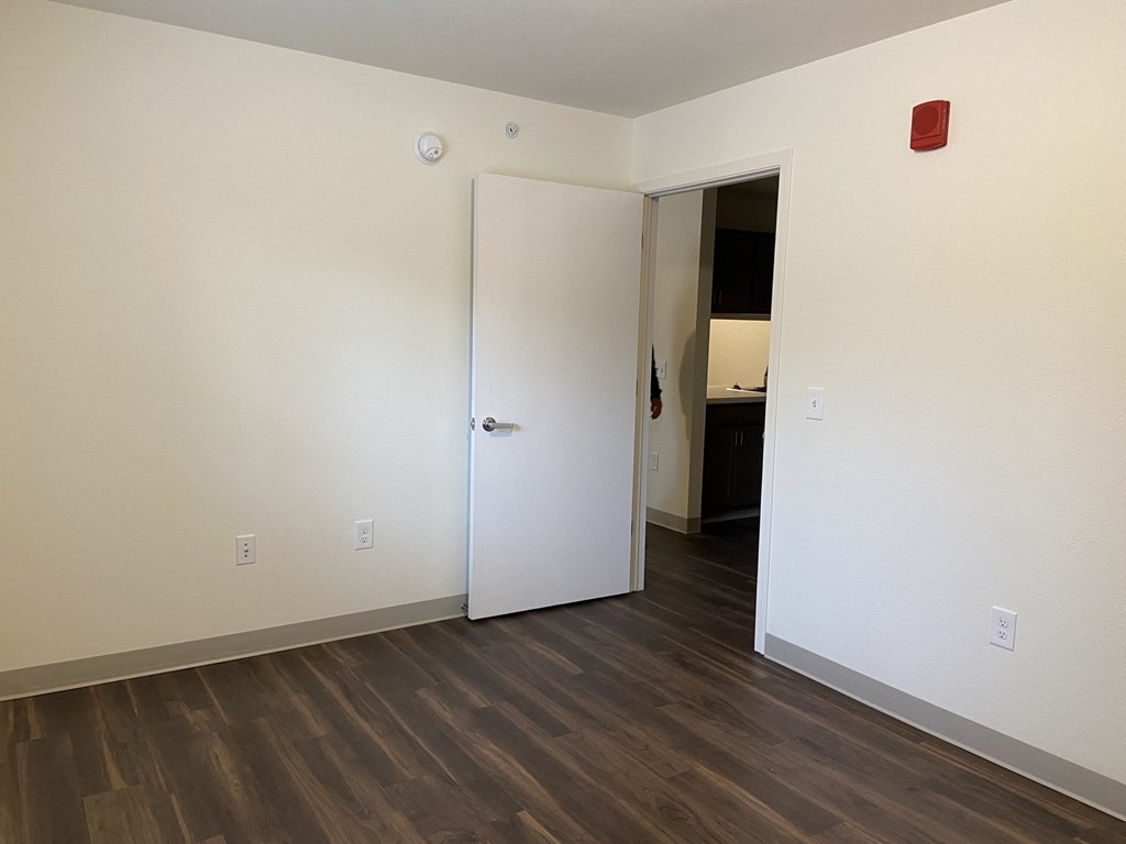 a bedroom with white walls and wood flooring and a door to a bathroom